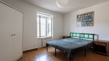 Ein Schlafzimmer mit Bett, Heizkörper, Fenster, Tür und Nachttisch.