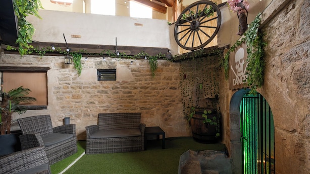 A rustic outdoor seating area with wicker furniture, a stone wall, and a green artificial turf floor.