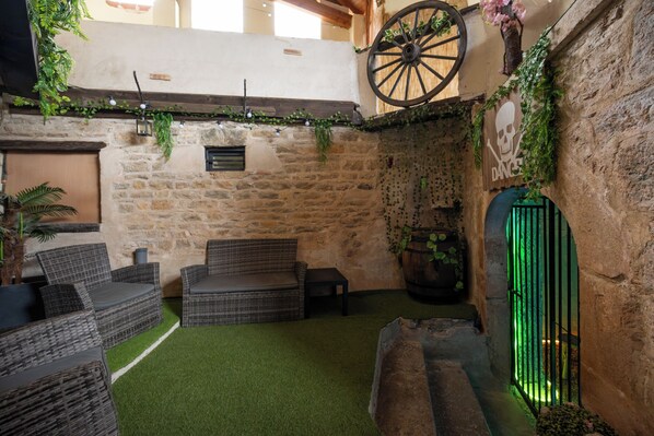 A rustic outdoor seating area with wicker furniture, a stone wall, and a green artificial turf floor.