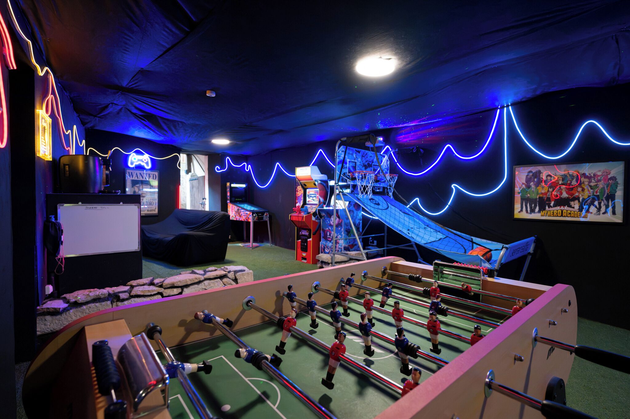 A room with a foosball table, a pool table, and a neon-lit wall.