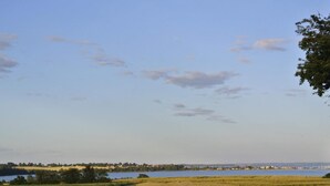 A rural landscape with a dirt path leading to a body of water, surrounded by fields and distant houses. - 6 Person Holiday Home in Hejls (Hejls)