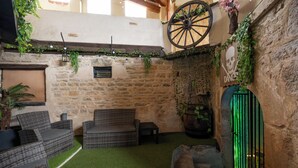 A rustic outdoor seating area with wicker furniture, a stone wall, and a green artificial turf floor. - 70 m² Loft for 4 People* in the Jura - Patio & Arcade Room (Val Suran)