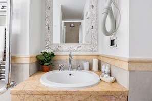 Baño con lavamanos blanco, espejo, secador de pelo y artículos de tocador.