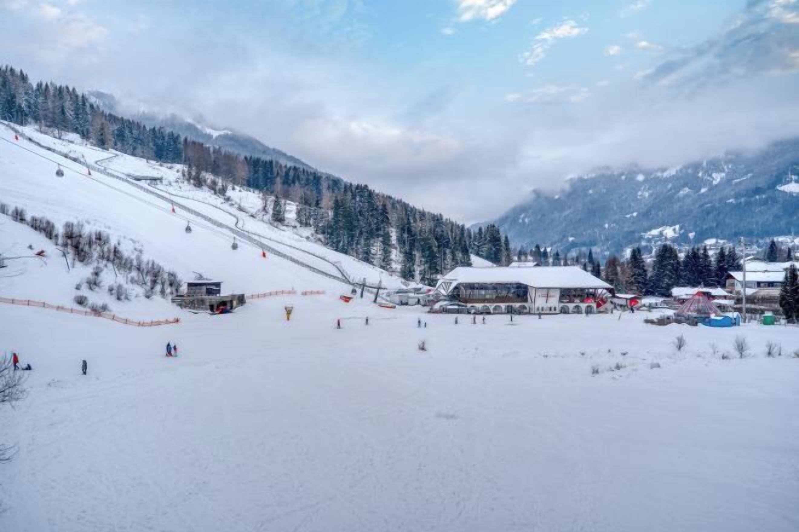 Une station de ski enneigée, avec un télésiège, des bâtiments et une montagne en toile de fond.
