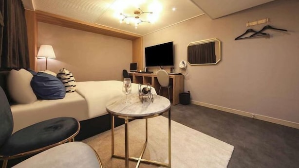 Une chambre d’hôtel avec un lit, un bureau, une télévision et une petite table sur laquelle se trouve un verre de vin.