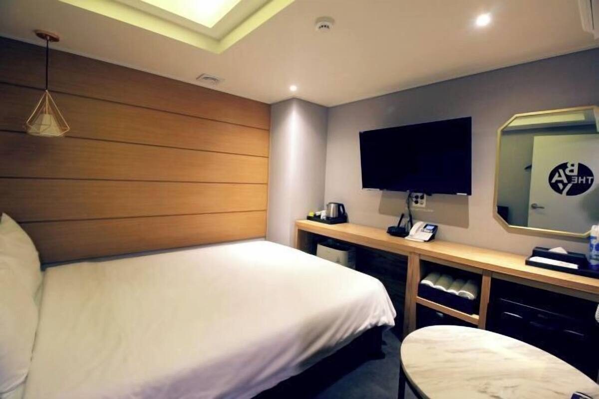 A hotel room with a bed, a desk, a chair, a TV, and a mirror.