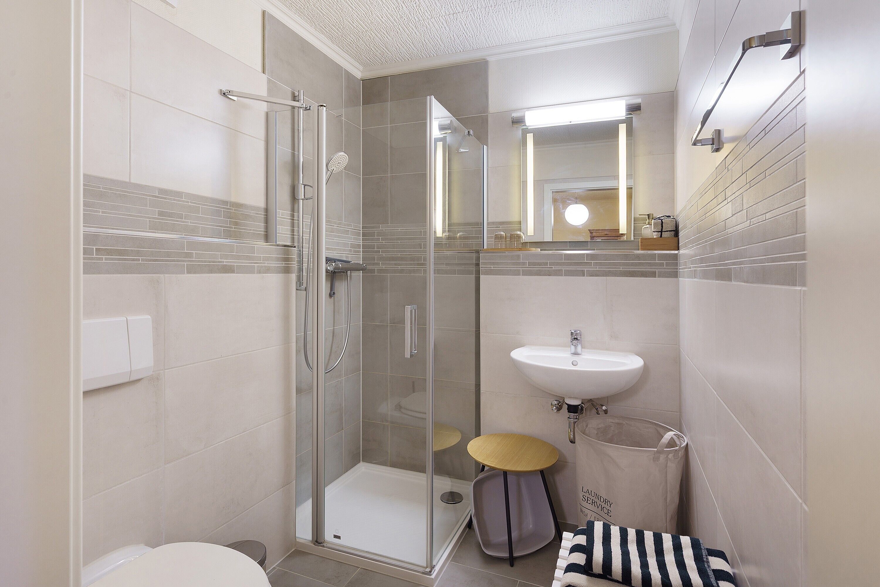 A bathroom with a glass shower enclosure, a sink, and a small round table.