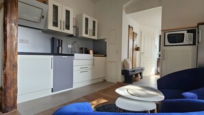 A compact kitchen with white cabinets, a microwave, a sink, and a small refrigerator. There is a blue chair and a round table with a woven placemat. - Apartment 2 'Near Blue Wonder' with Shared Terrace, Garden and Wi-Fi (Dresden)