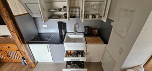 Une cuisine compacte dotée d’une plaque de cuisson à induction noire, de meubles blancs et d’un plan de travail en bois.