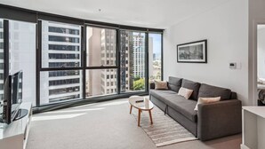 Ein modernes Wohnzimmer mit grauem Sofa, einem weißen Couchtisch und einem großen Fenster mit Blick auf die Stadt.