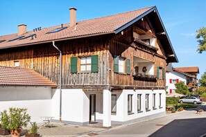 A traditional wooden house with a balcony, a white facade, and a red-tiled roof.