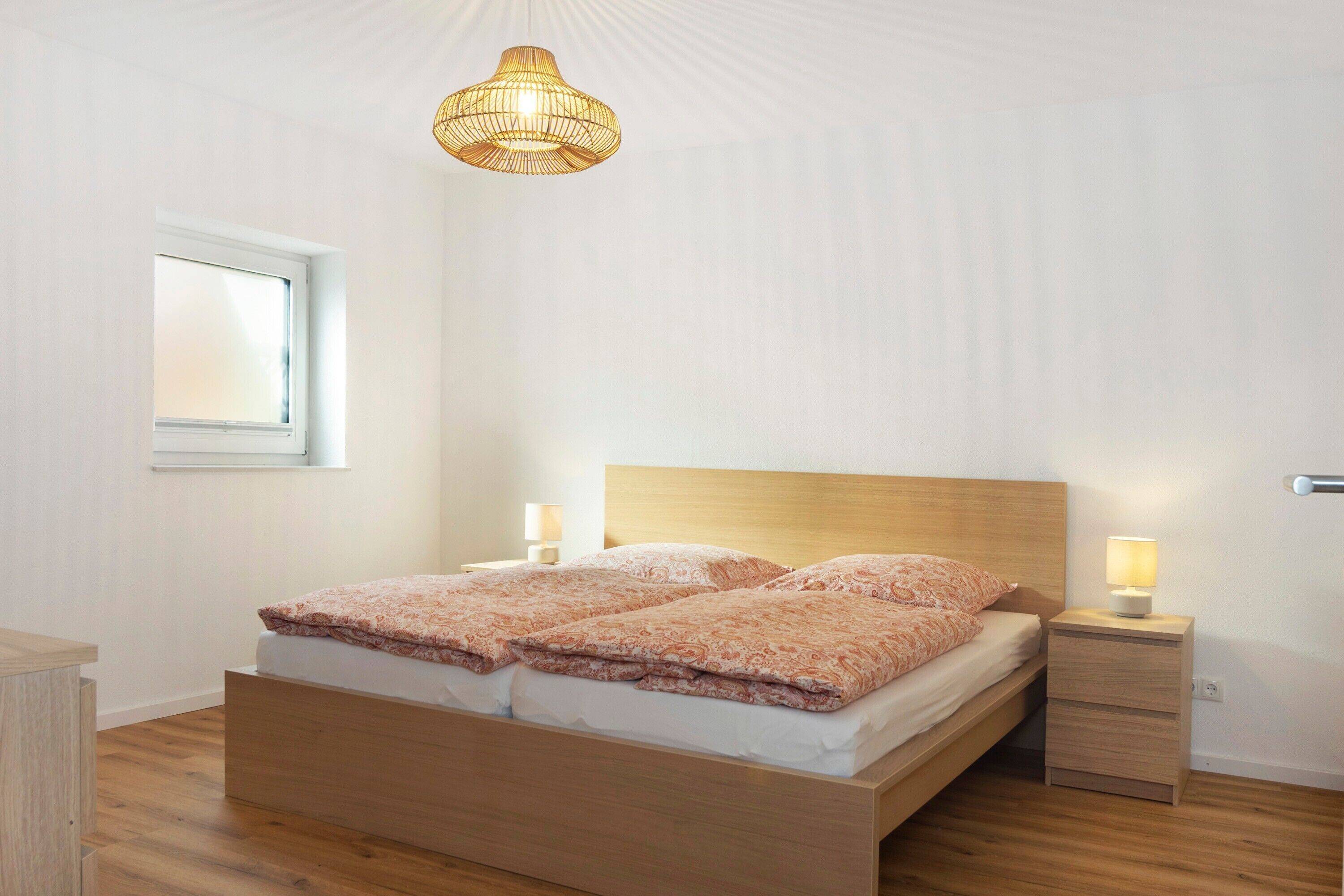 A bedroom with a wooden bed, bedside tables, a hanging light fixture, and a window.