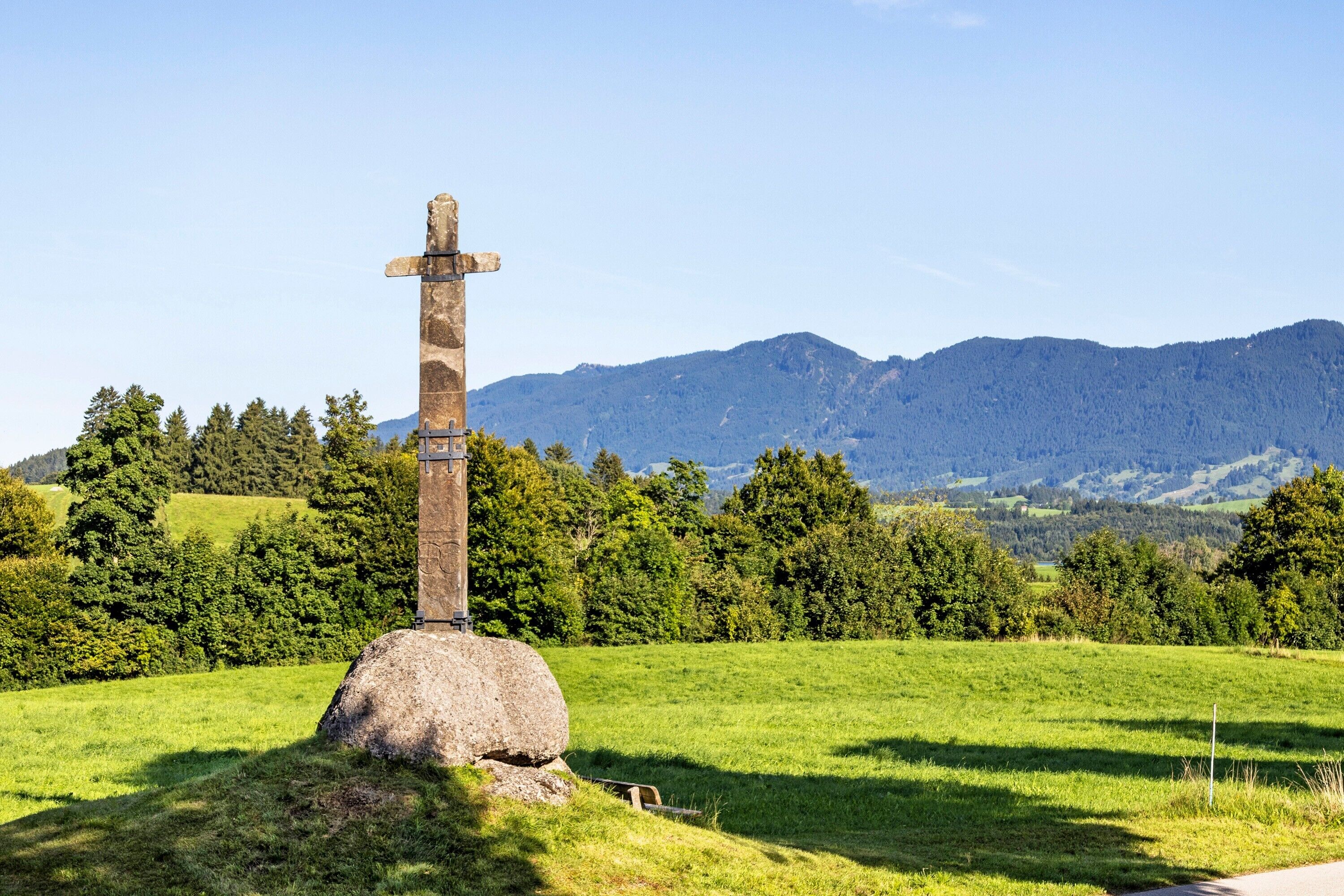 Una cruz de piedra en un campo cubierto de hierba, con montañas al fondo.