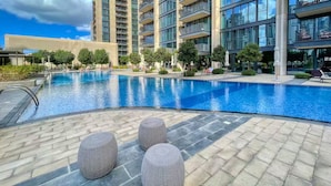 A swimming pool with lounge chairs and ottomans, surrounded by modern buildings. - BLVD Heights Residences - Downtown (Dubai)