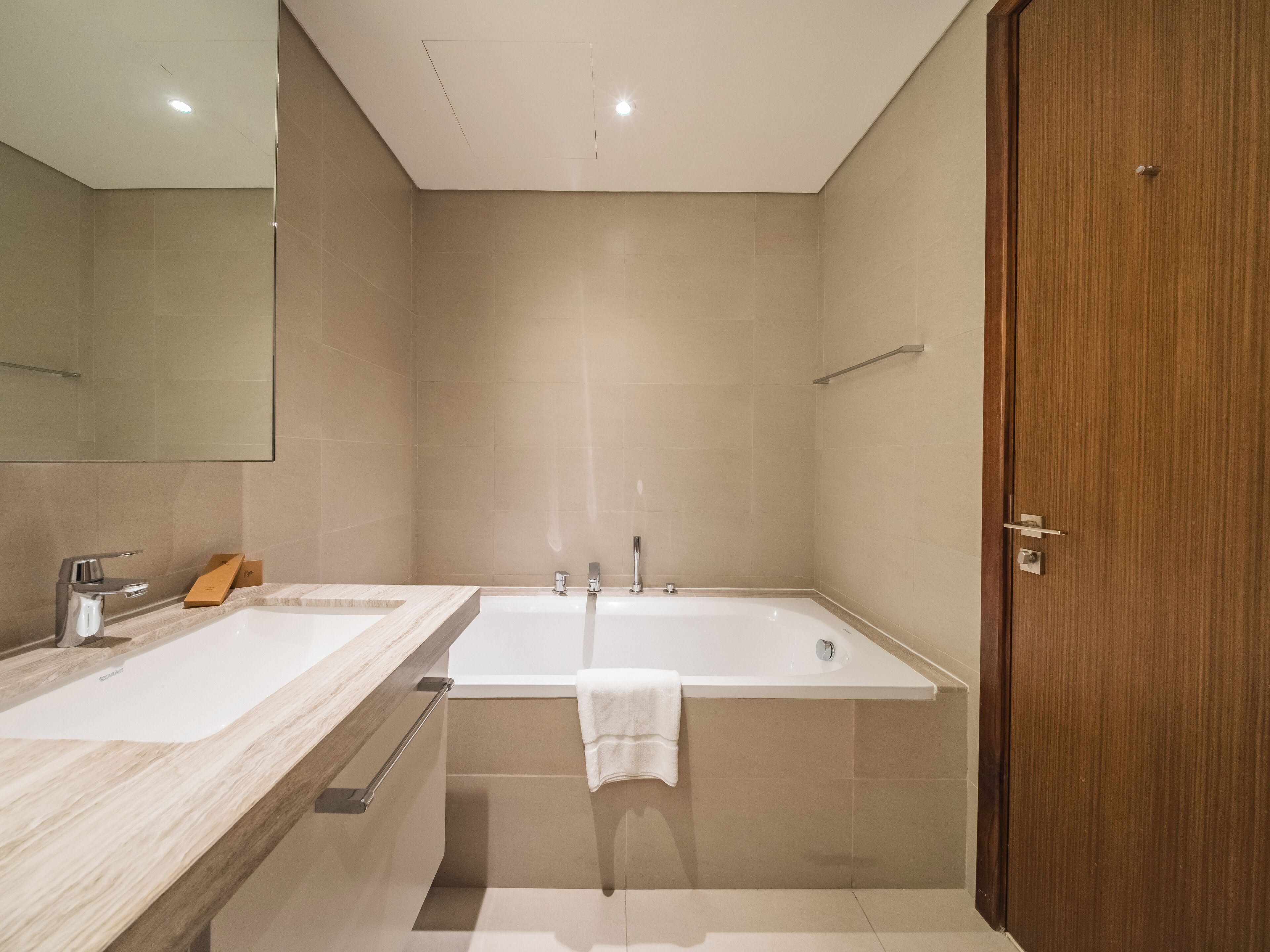 A modern bathroom with two sinks, a large bathtub, and a wooden door.