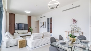 A modern living room with a sofa, ottoman, and a dining area with a glass table and chairs. - BLVD Heights Residences - Downtown (Dubai)