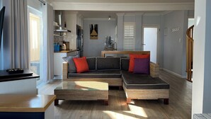 A modern living room with a sectional sofa, a glass coffee table, and a wooden floor. - 8@Lalandi Beachfront Cottage Langstrand 15km between Swakopmund & Walvis Bay (Langstrand)