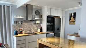 A modern kitchen with a central island, built-in appliances, and a dining area with bar stools. - 8@Lalandi Beachfront Cottage Langstrand 15km between Swakopmund & Walvis Bay (Langstrand)