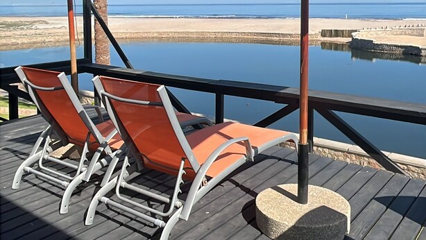 A wooden deck with lounge chairs and umbrellas overlooking a beach and calm sea. - 8@Lalandi Beachfront Cottage Langstrand 15km between Swakopmund & Walvis Bay (Langstrand)