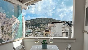 Uma varanda com mesa, cadeiras, um vaso de planta e dois copos de vinho branco.
