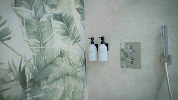 A bathroom with a shower, two bottles of shampoo and shower gel, and a wall with a leafy pattern.