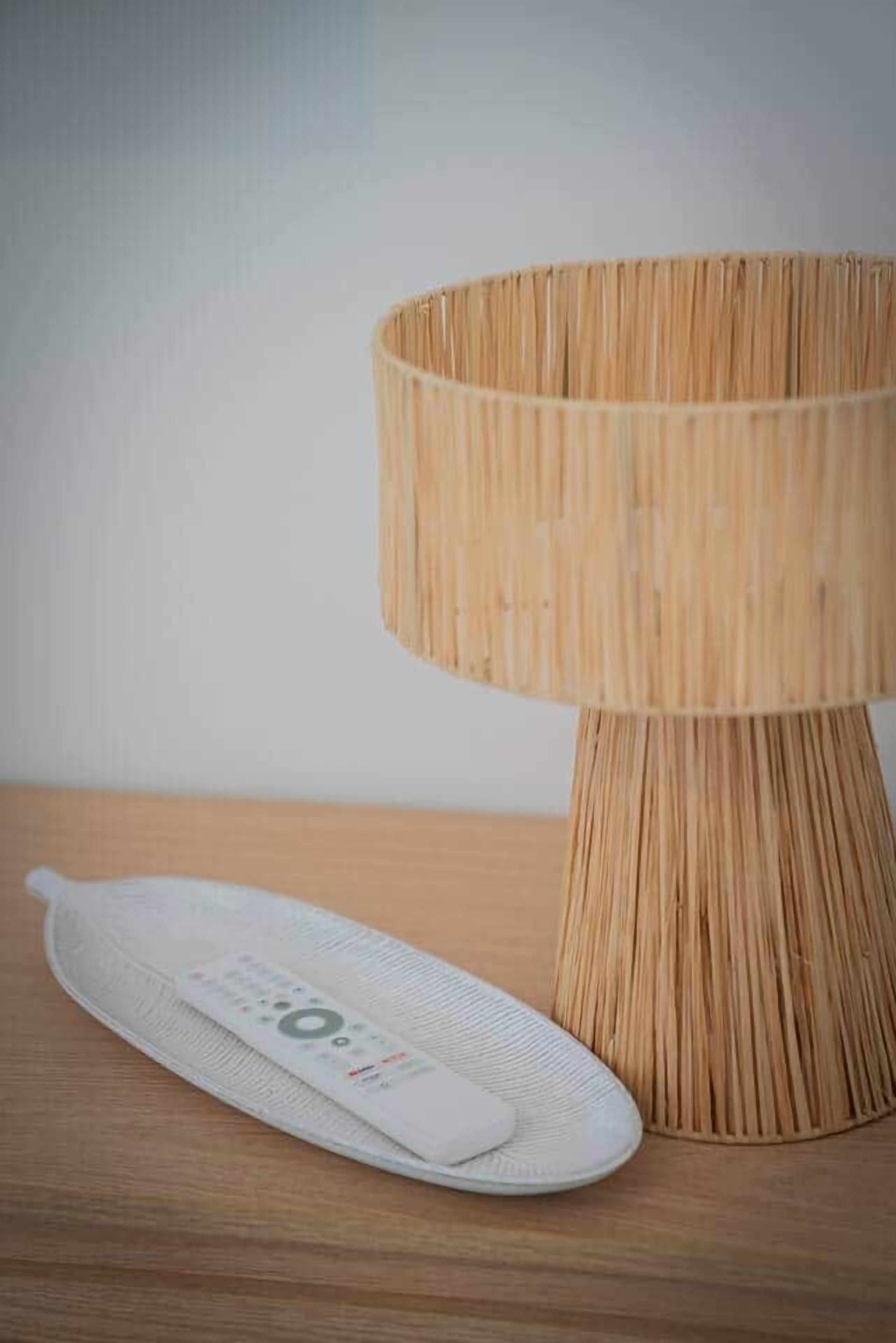 Eine runde, gewebte Tischlampe mit weißem Fuß und einem weißen Gegenstand daneben.