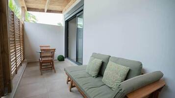 Une terrasse couverte avec un plafond en bois, un canapé vert avec des coussins, une chaise en bois et une petite table.