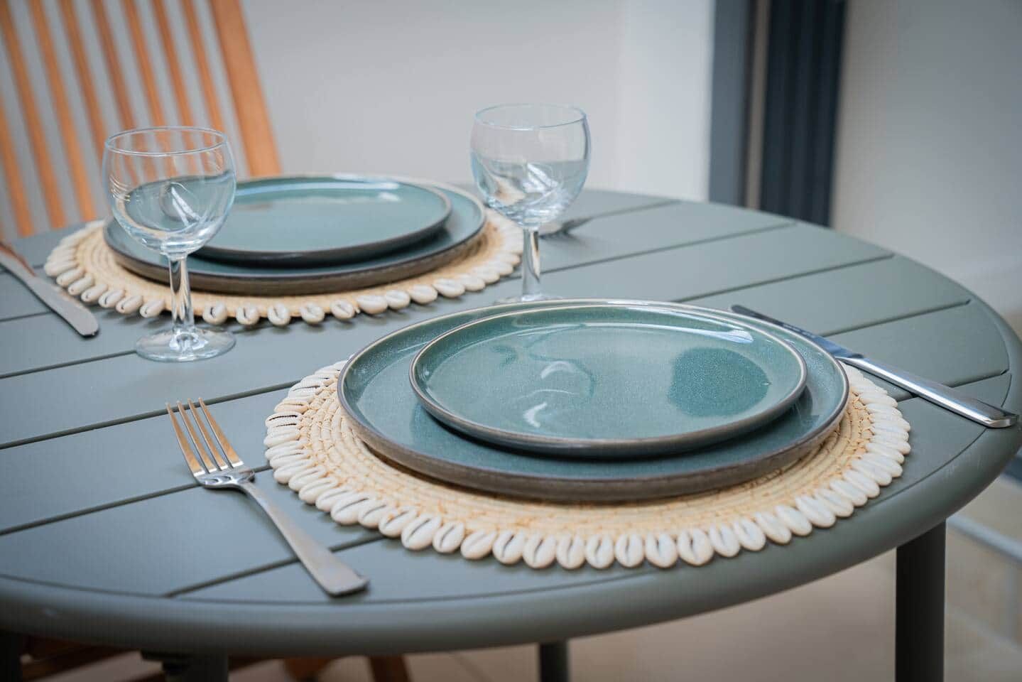 Une table dressée avec deux assiettes, deux verres à vin, une fourchette et un couteau.