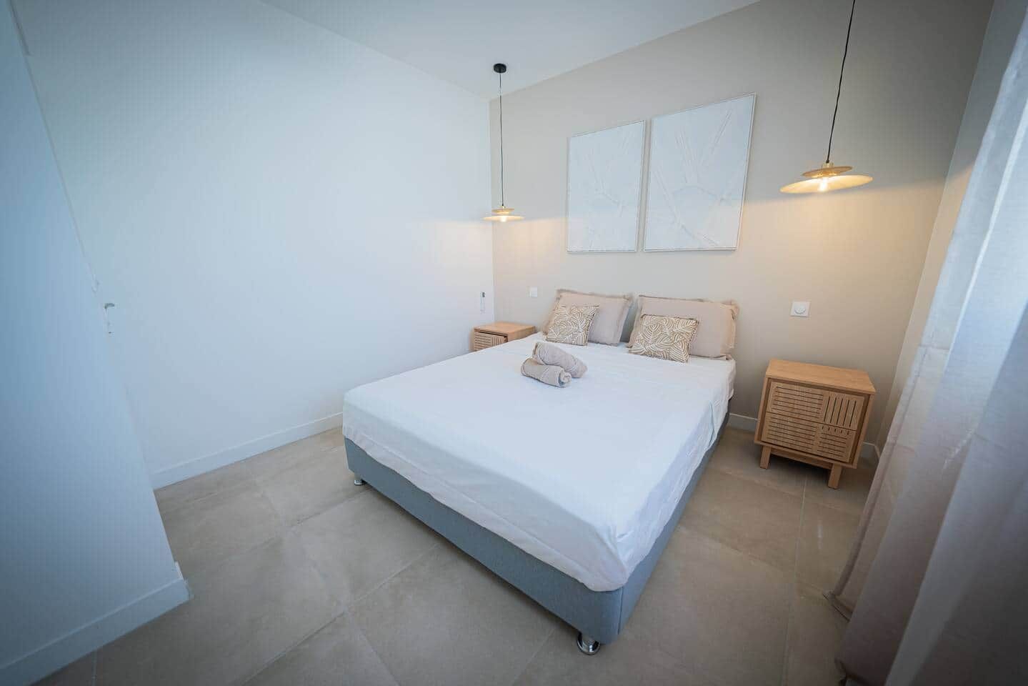 Une chambre à coucher comprenant un lit, deux tables de chevet et deux lampes fixées au mur.