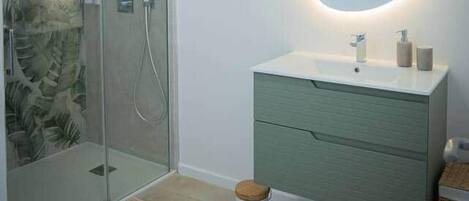 Une salle de bain moderne dotée d’une douche à parois de verre, d’un meuble-lavabo vert et d’un miroir rond avec éclairage intégré.
