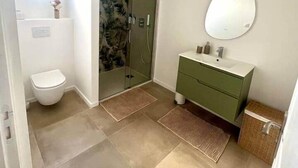 A bathroom with a toilet, a shower, and a vanity with a mirror.