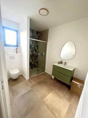 Un baño con inodoro, ducha y tocador con espejo.