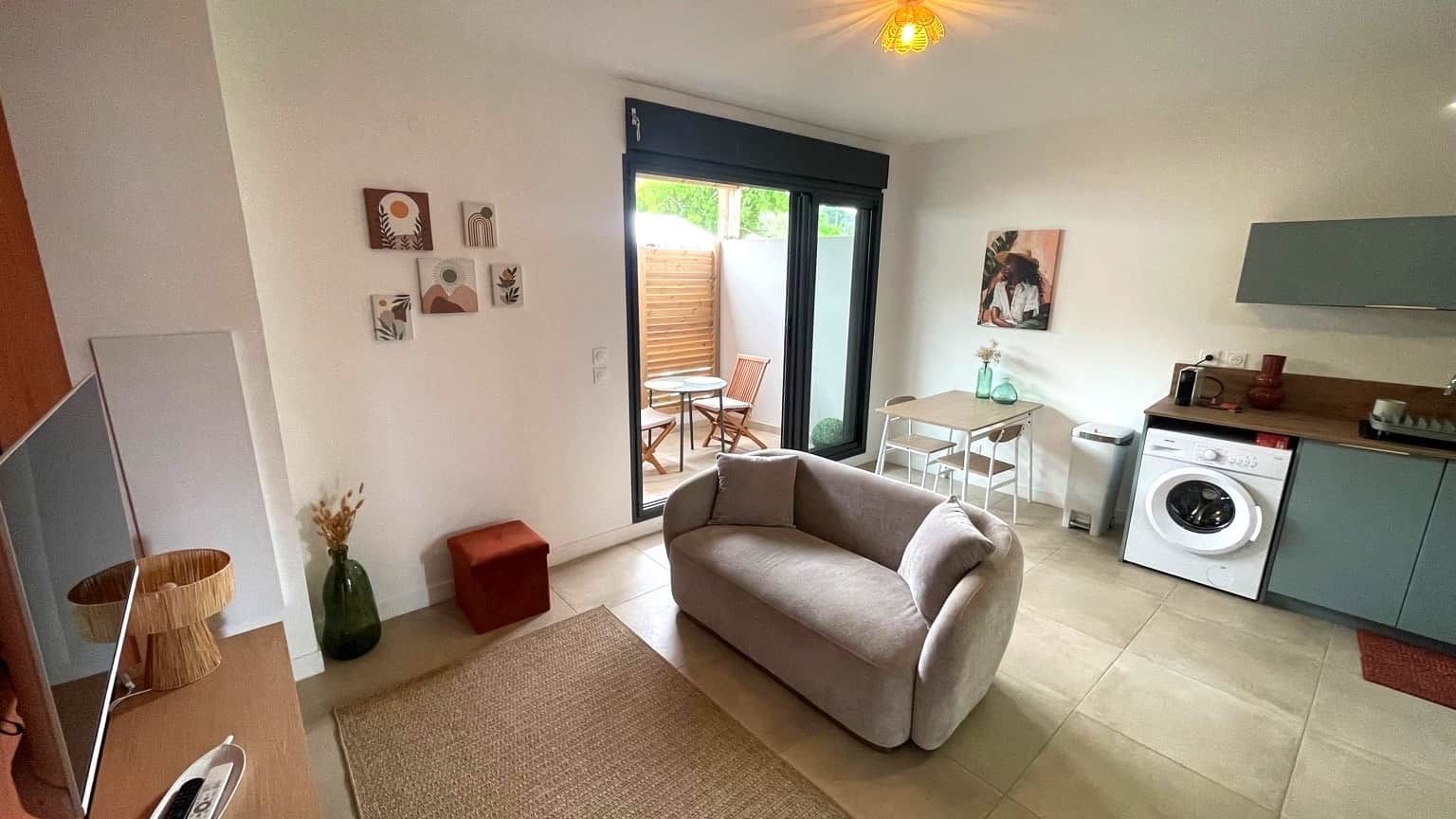 Ett kompakt bostadsutrymme med en soffa, en matplats, en tvättmaskin och en TV.