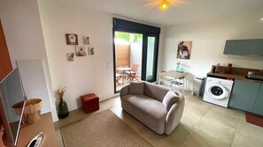 A compact living space with a sofa, a dining area, a washing machine, and a TV.