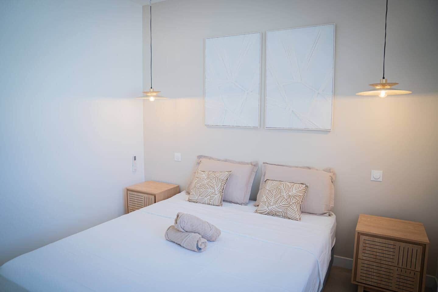 A bedroom with a bed, two bedside tables, and two wall-mounted light fixtures.