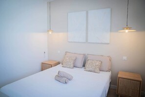 A bedroom with a bed, two bedside tables, and two wall-mounted light fixtures.