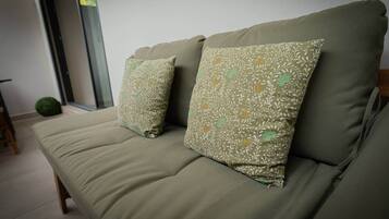 Un sofá con dos cojines estampados en una habitación con un ventanal y una pequeña planta verde.