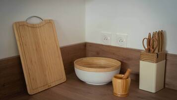 Una encimera de cocina con una tabla de cortar de madera, un tazón blanco, una cuchara de madera en un portalápices y un bloque de cuchillos.