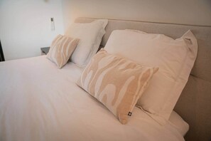 A bed with beige bedding and two pillows, one with a striped pattern and the other plain.