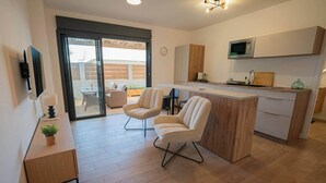 A modern kitchen with a wooden island, a dining area with two chairs, and a sliding glass door leading to an outdoor patio. - Cosy T2 - La Verrière (La Possession)