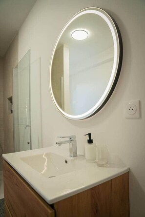 A bathroom with a round mirror, a white sink, and a wooden cabinet.