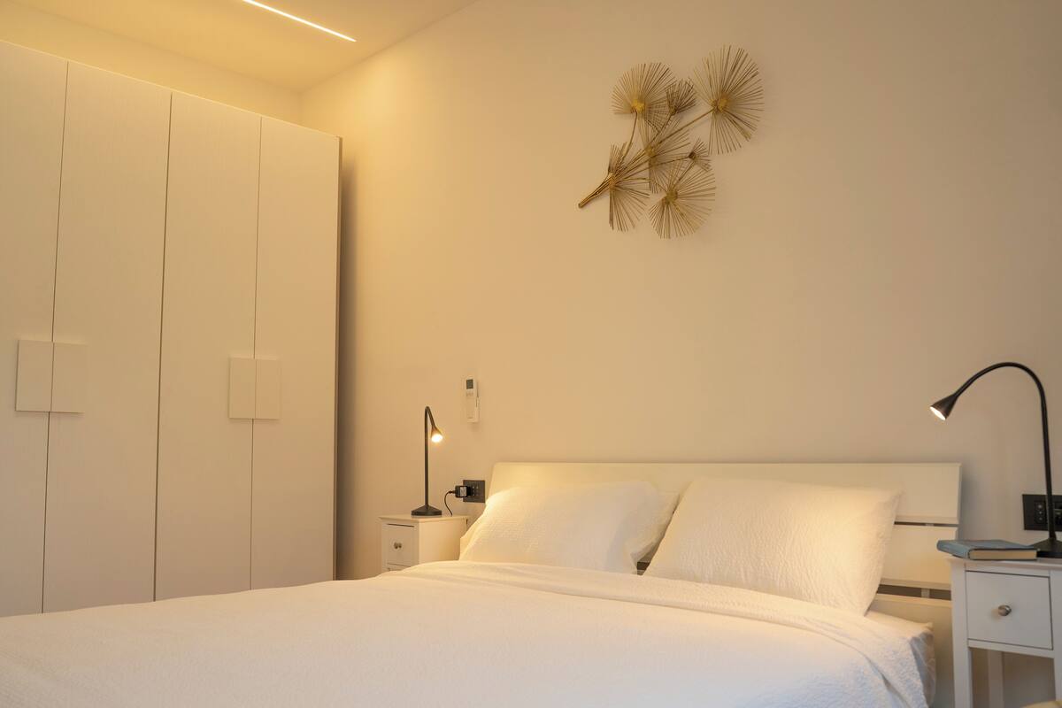 A neatly arranged bedroom with a bed, bedside tables, a wardrobe, and a wall-mounted light fixture.
