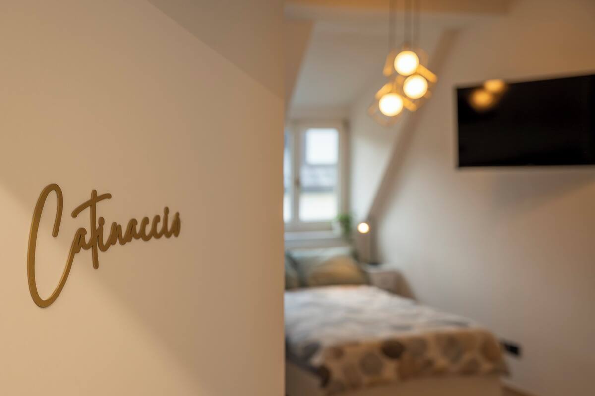A bedroom with a bed, a hanging light fixture, and a wall with the name 'Cafinacci' written on it.