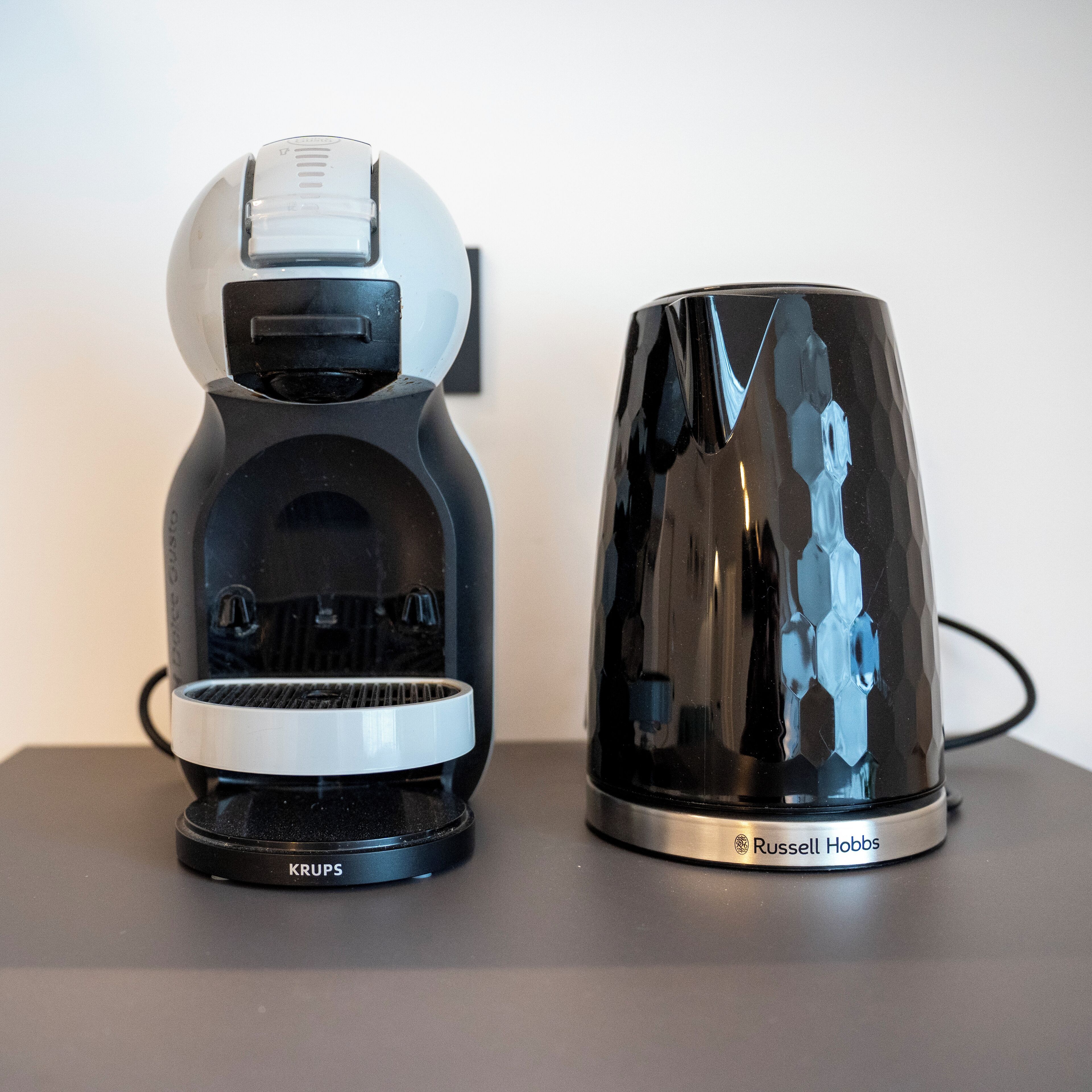 Two coffee makers, one labeled KRUPS and the other Russell Hobbs, placed on a flat surface.