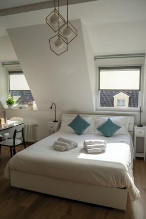 A bedroom with a large bed, two bedside tables, a desk, and a chair. There are two windows with a view of a house. - Talvera Dream (Bolzano)