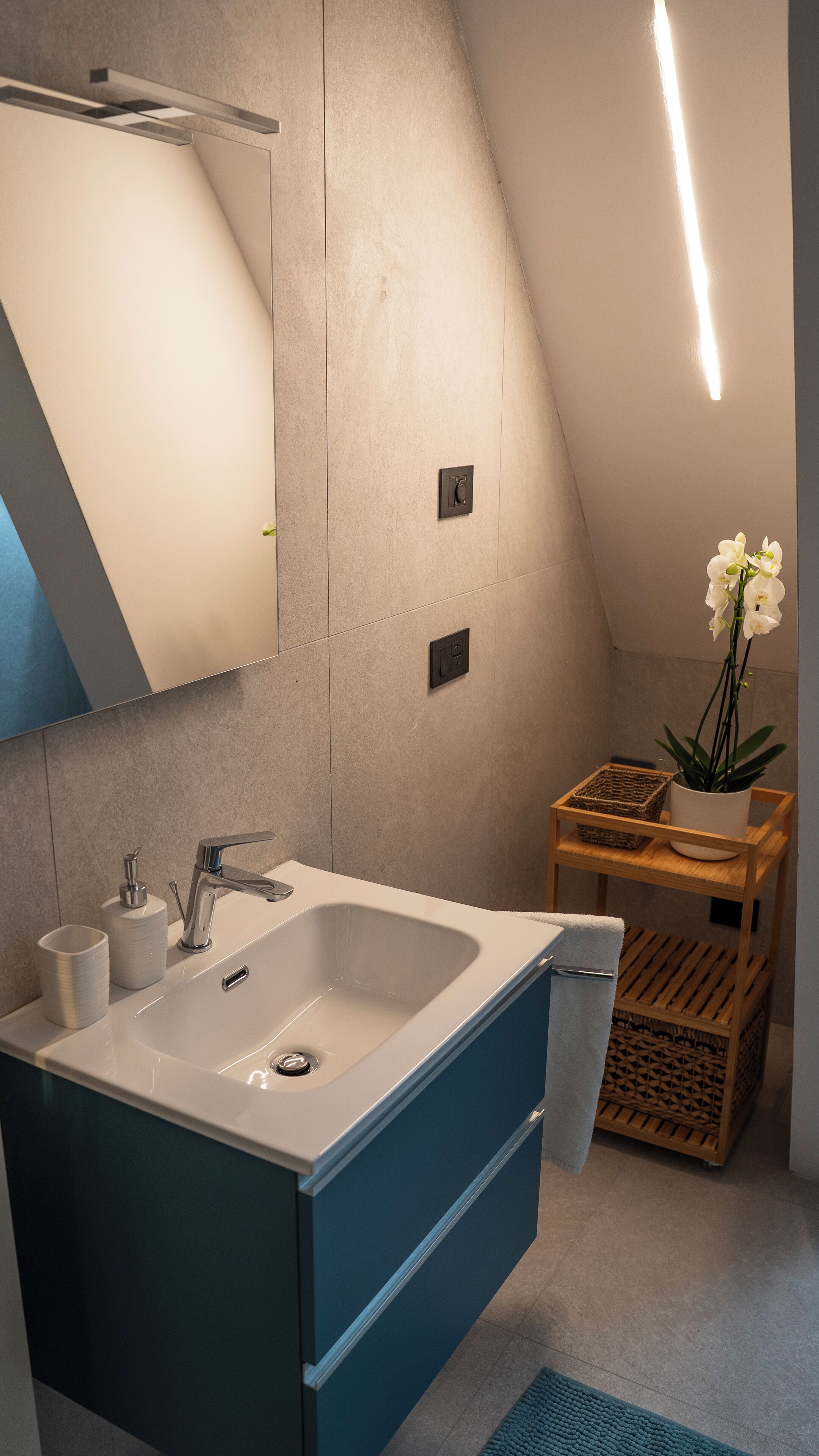 Un baño moderno con un lavamanos blanco, armarios azules y un tocador de madera.