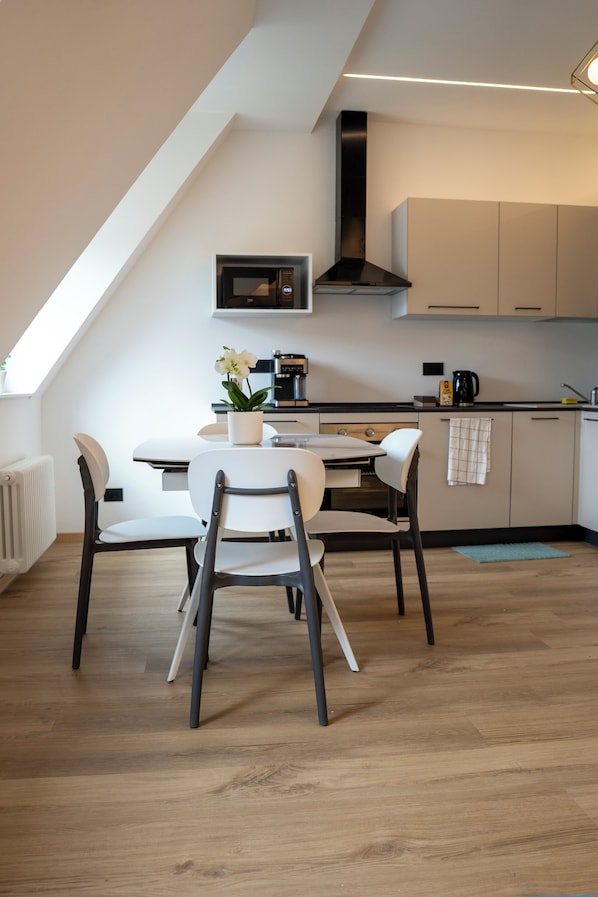 A modern kitchen with a dining area, featuring a white table, chairs, and a potted plant. - Talvera Dream (Bolzano)