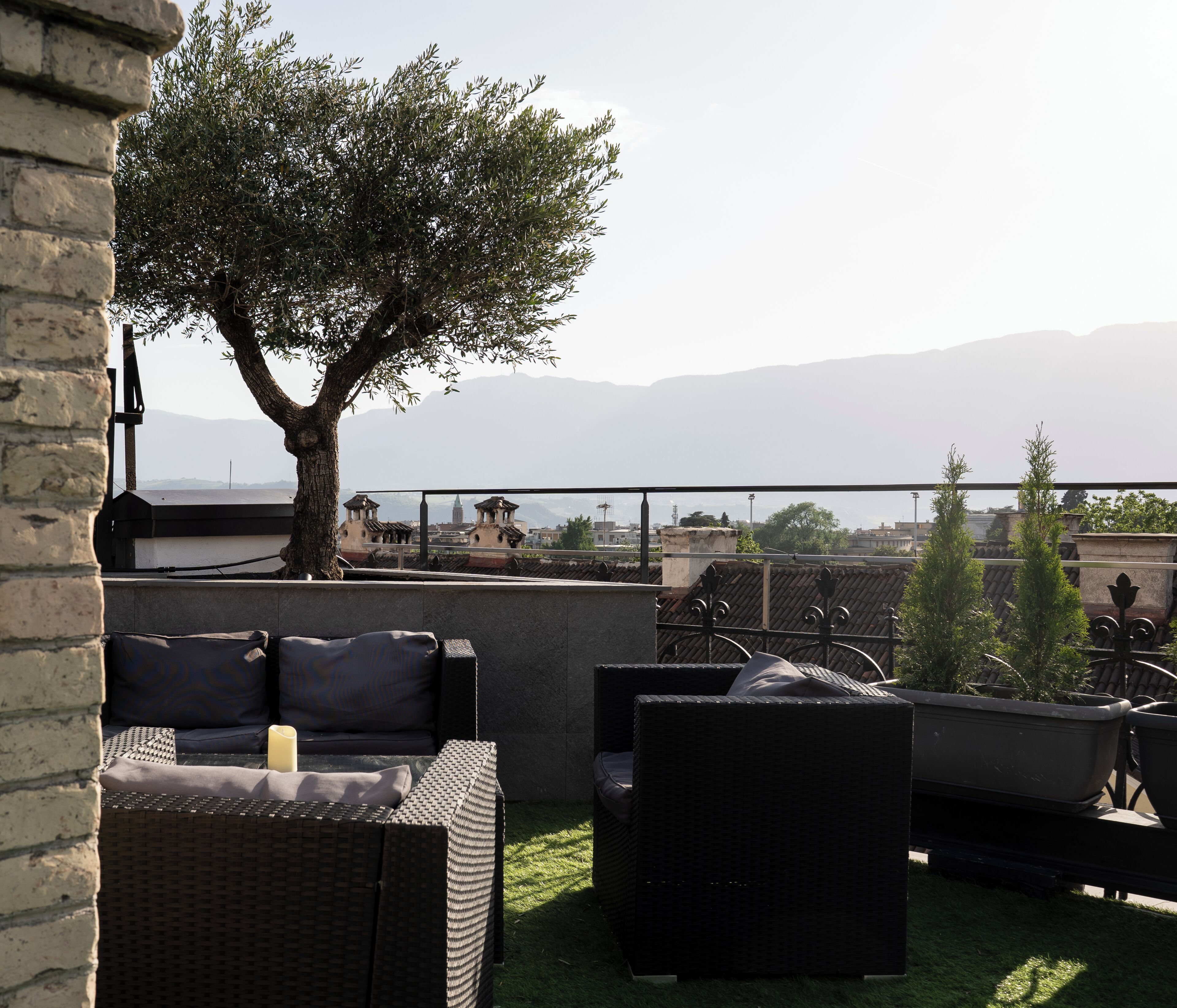 A rooftop terrace with outdoor furniture, a tree, and a view of distant mountains.
