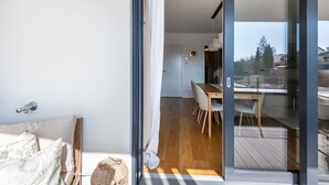 A modern room with a sliding glass door leading to a balcony, a wooden floor, and a dining area with chairs. - Apartment 'Bei Stefanie' with Mountain View, Balcony and Wi-Fi (Bad Kötzting)