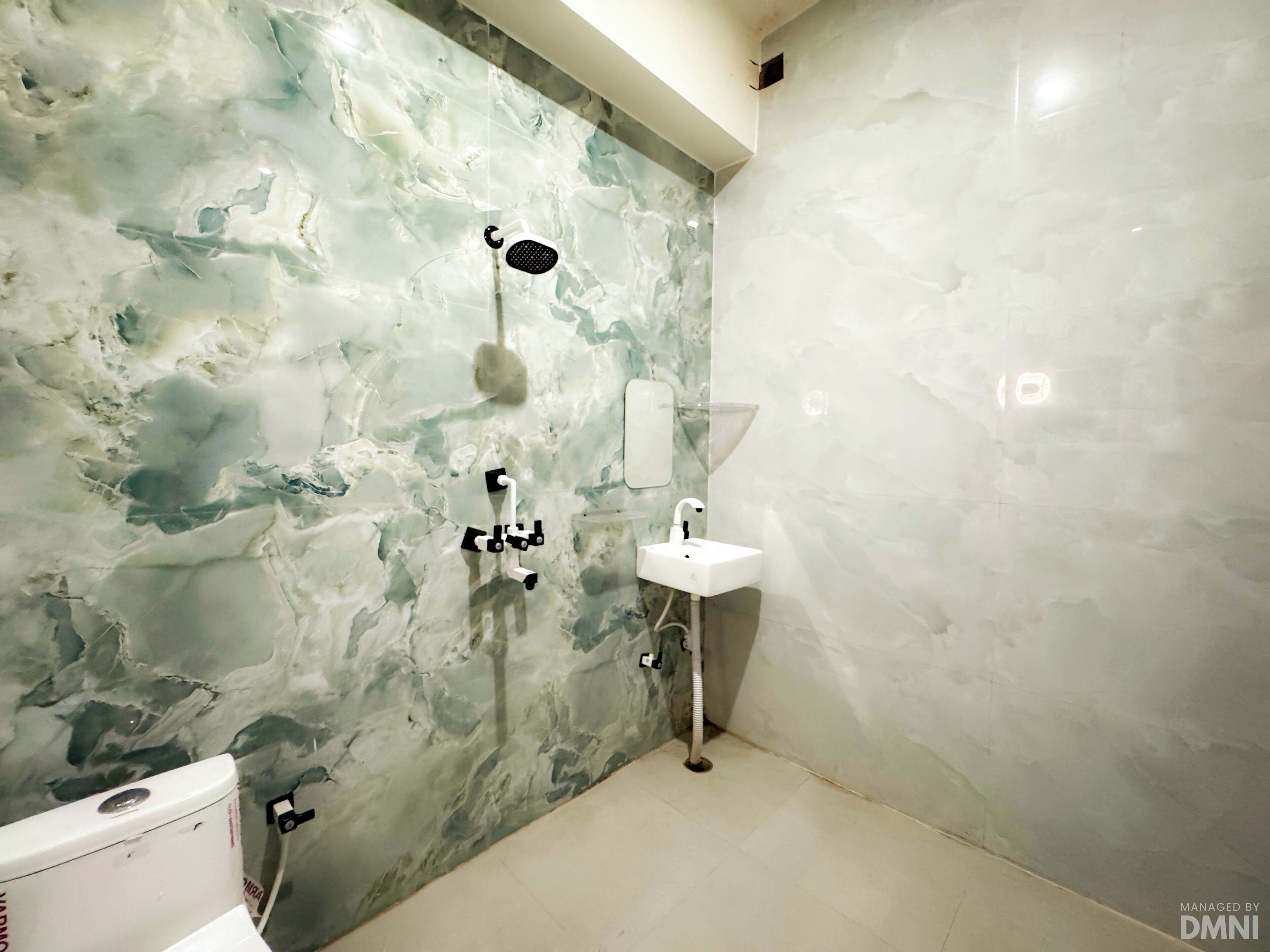 A bathroom with a marble wall, a shower, a sink, and a toilet.